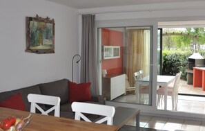 A modern living room with a sofa, dining table, and chairs. There is a sliding glass door leading to an outdoor patio with a barbecue grill. - Lakeside apartment with enclosed garden, dog allowed, electric charger (Hourtin)