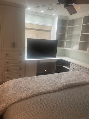 Un dormitorio con cama, televisor, estanterías empotradas y ventilador de techo.