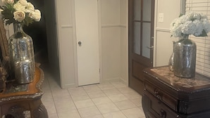 Un pasillo con una puerta, un espejo y un jarrón de flores sobre una mesa de madera.