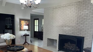 Un salón comedor espacioso con suelo de madera, chimenea, araña y mesa con sillas.