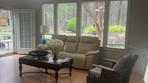 Un salón amplio con un gran ventanal, una araña, un sofá color beige, un sillón estampado y una mesa de centro de madera.