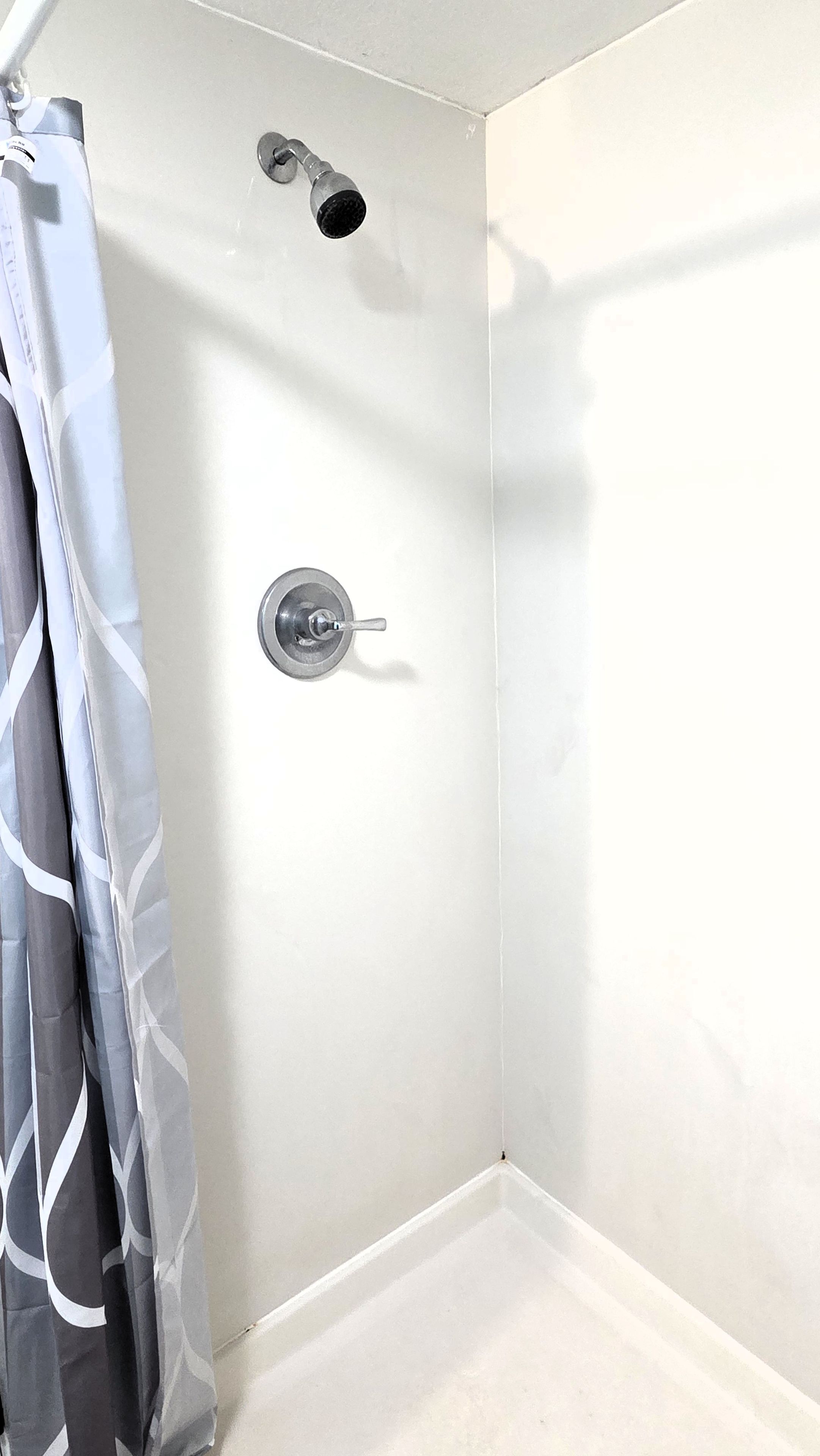 Une douche d’angle avec un mur blanc, un pommeau de douche et un rideau.