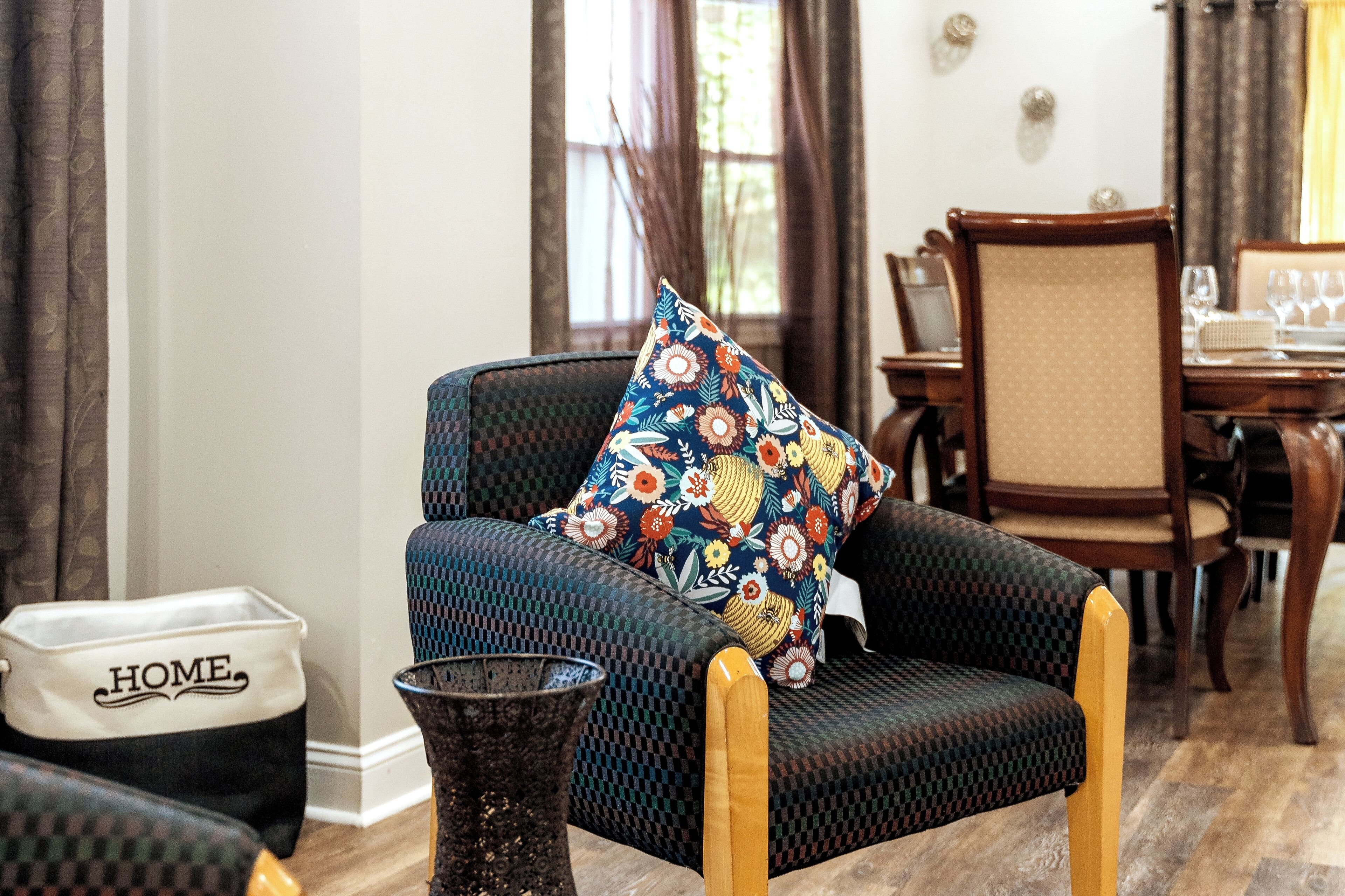 A living room with a patterned armchair, a dining table set with chairs, and a decorative vase.