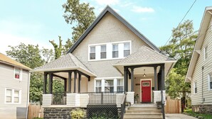 A two-story house with a red front door, a covered porch, and a stone foundation. - Tudor Lux (East Lansdowne)