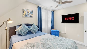 A bedroom with a bed, a ceiling fan, a TV displaying 'NETFLIX', and a painting on the wall.