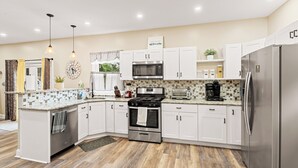 A modern kitchen with white cabinets, stainless steel appliances, and a tiled backsplash. - Tudor Lux (East Lansdowne)
