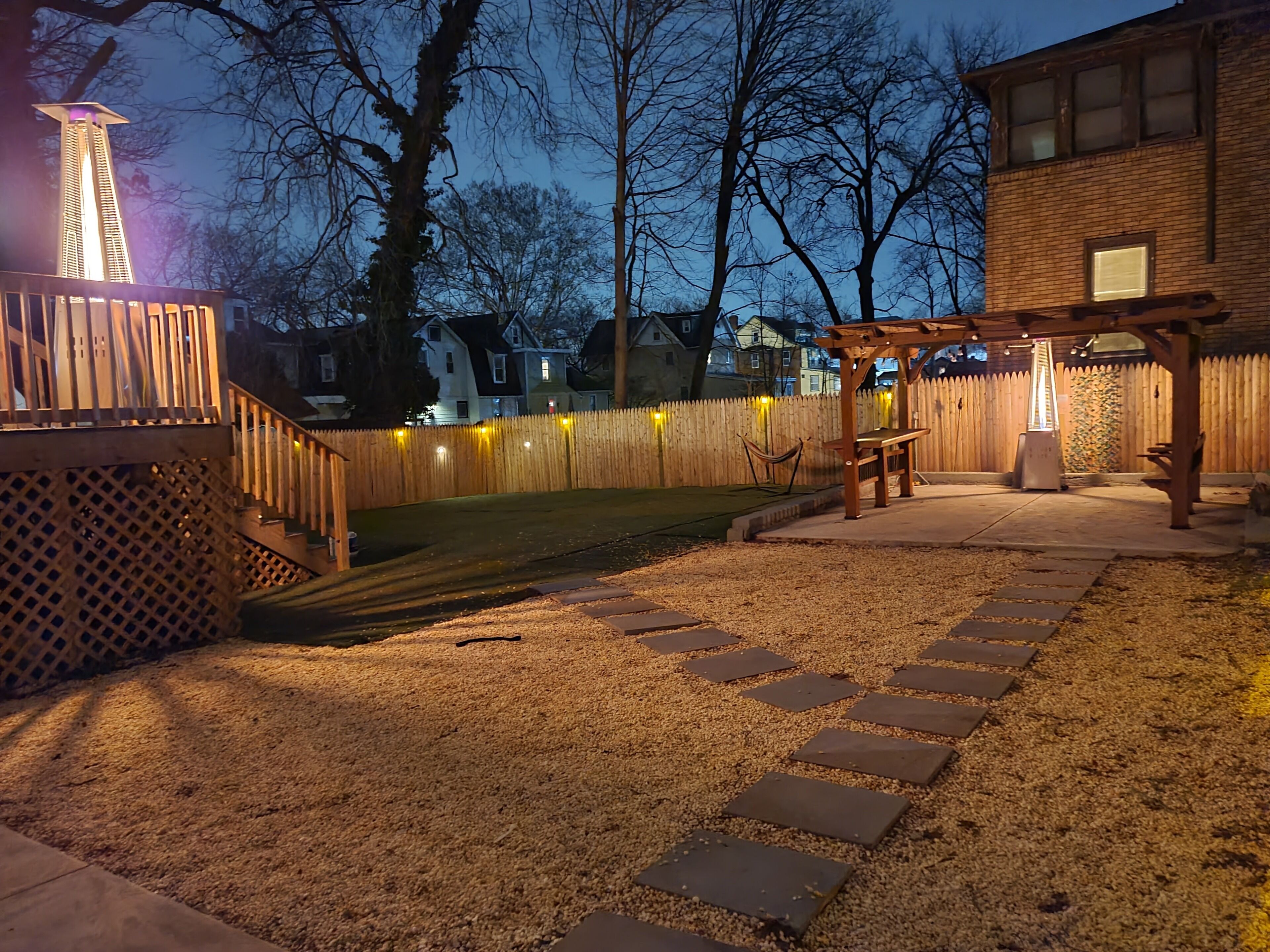 A backyard with a wooden deck, a pergola, and a gravel pathway.