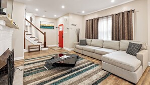 A living room with a sofa, a coffee table, a fireplace, a staircase, and a painting on the wall. - Tudor Lux (East Lansdowne)