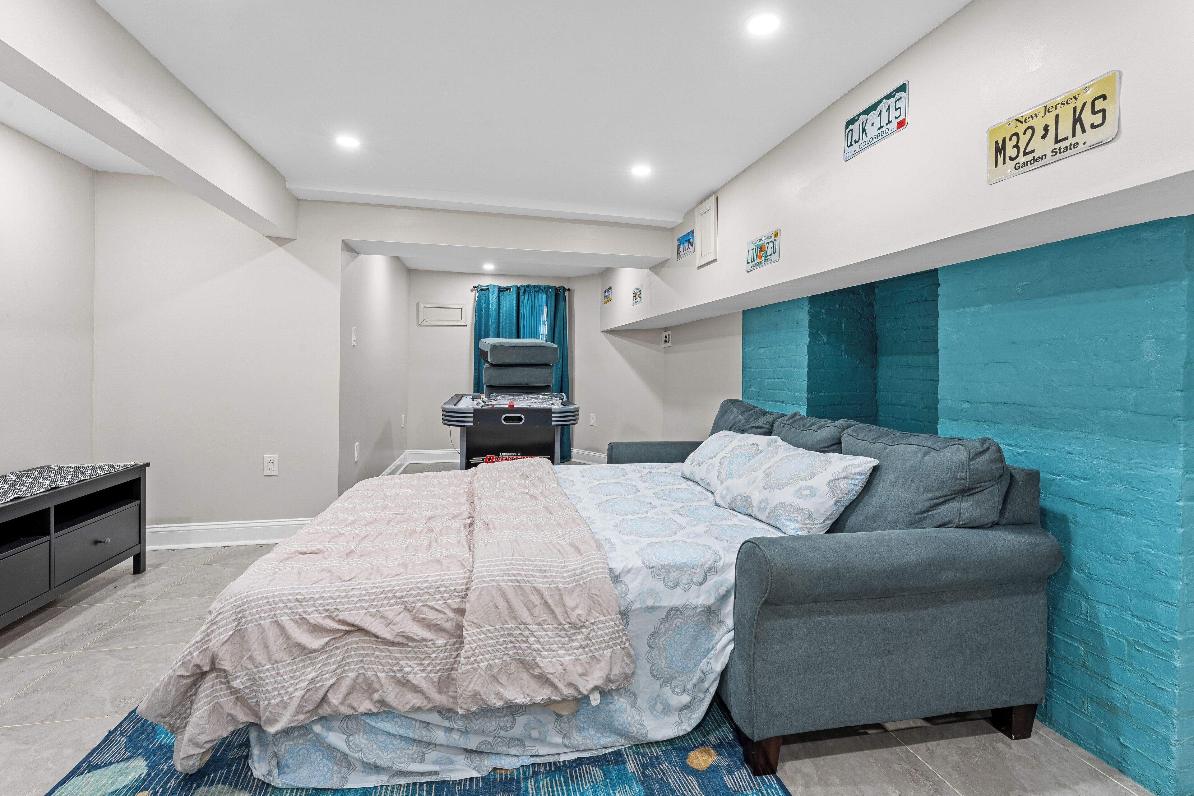 A bedroom with a bed, a grey sofa, a desk with a computer, and a blue wall.