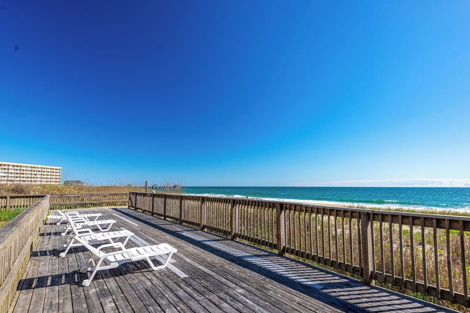 Een houten terras met witte ligstoelen met uitzicht op een strand.