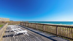 Une terrasse en bois avec des chaises longues blanches donnant sur une plage.