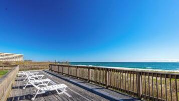 Een houten terras met witte ligstoelen met uitzicht op een strand.