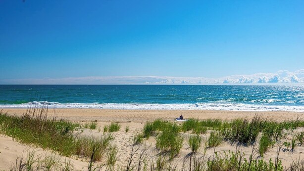 Une plage avec des dunes de sable et une personne assise sur une serviette.