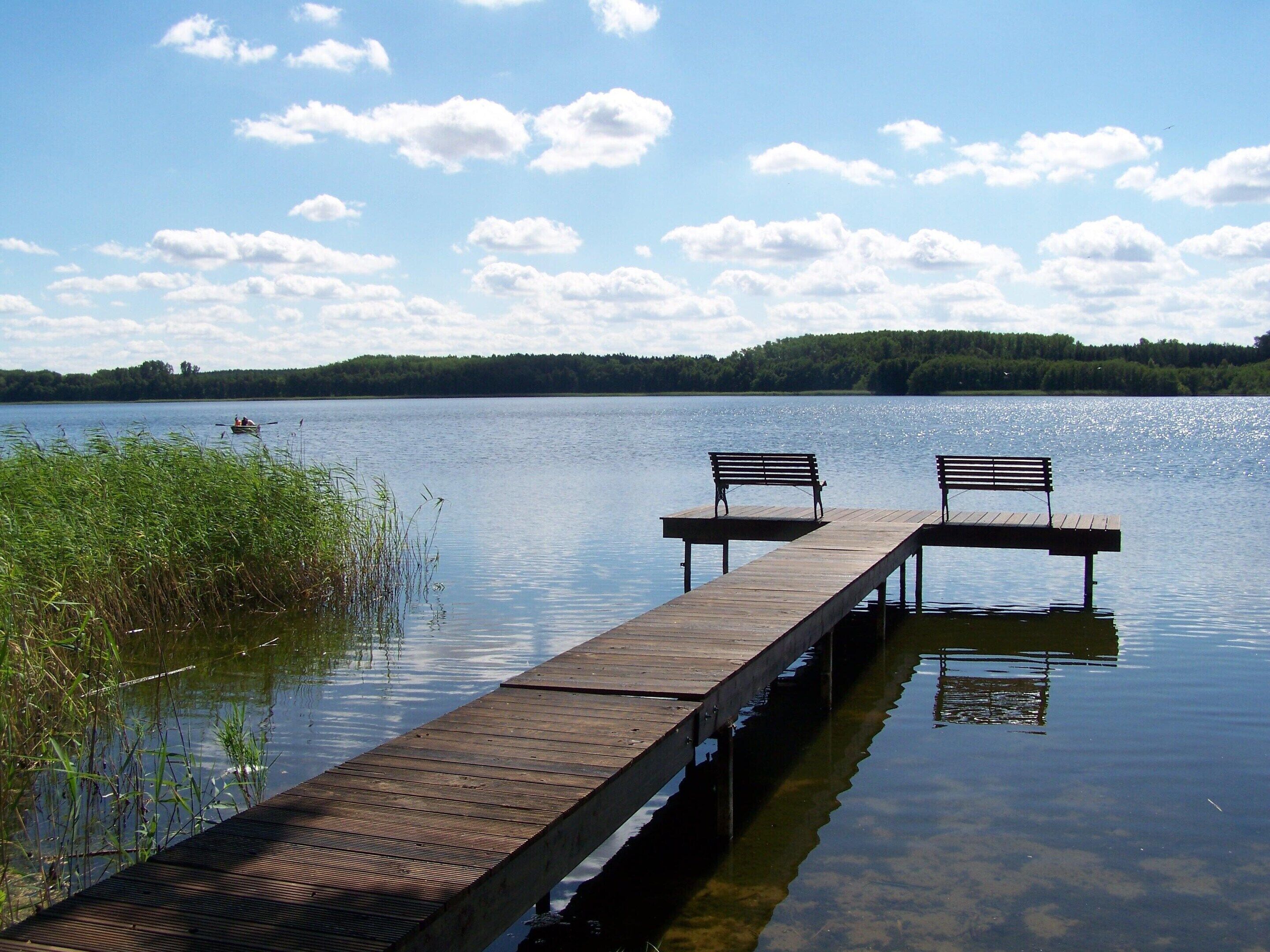 A wooden pier extending into calm water with two benches facing the water.