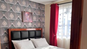 Un lit bien fait, avec du linge de lit blanc, une tête de lit en bois et un tapis à motifs sur le sol.