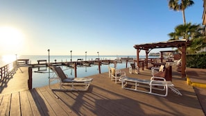 A wooden deck with lounge chairs and a covered seating area overlooking a calm body of water. - NEW! Direct Bayfront Sunsets - Boat Docks - Pool - Fish (South Padre Island)