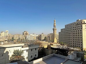 A cityscape with a prominent minaret, modern buildings, and a rooftop terrace. - Lovely 2-bedroom apartment in Cairo downtown overlooking Tahrir Square in . (cairo -downtowwn -Qasr El-Nil District)