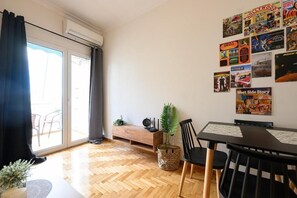 Un comedor con suelo de madera en dibujo de espiga, una mesa negra con sillas, una planta y una pared decorada con varios carteles.