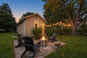 A backyard with a fire pit, two Adirondack chairs, and a string of lights. - 2BR Cottage w/ Backyard | 10 Min Walk to Kirkwood (Bloomington)