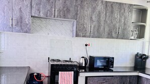 A modern kitchen with grey cabinets, a black stove, a microwave, and a gas cylinder. - A Calm, Elegant 3BR retreat in Milimani, Kitale (Kitale)