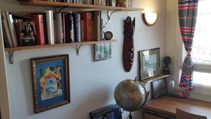 Ein Zimmer mit Schreibtisch, Regalen mit Büchern, einem Globus und einem gerahmten Bild.