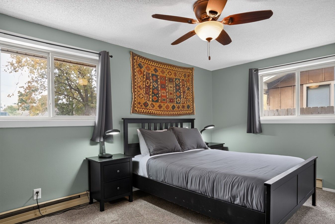 A bedroom with a bed, nightstands, a ceiling fan, and a window with curtains.