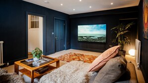 Een moderne woonkamer met een grote flatscreen-tv, een houten salontafel, een zacht vloerkleed en een bank met kussens.