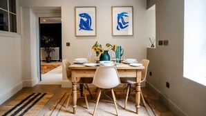 Een eethoek met een houten tafel gedekt voor vier personen, twee ingelijste kunstwerken erboven en uitzicht op een woonruimte.