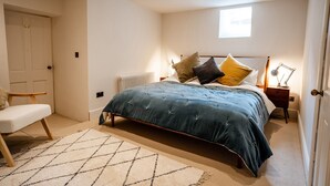 Een slaapkamer met een bed, nachtkastje, lamp, stoel en een radiator.