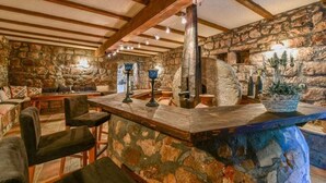 A rustic interior with stone walls, wooden beams, a stone fireplace, and a bar area with stools and a potted plant. - Authentic Mediterrannean Villa Ancient Mill with Swimming Pool and Sea View (Luštica)
