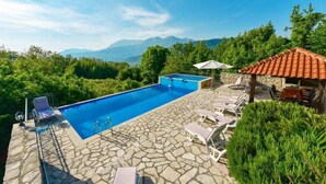A swimming pool with stone flooring, surrounded by lounge chairs and a stone building with a tiled roof. - Authentic Mediterrannean Villa Ancient Mill with Swimming Pool and Sea View (Luštica)
