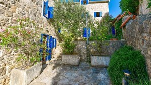 A narrow stone pathway flanked by buildings with blue shutters, leading to a stone wall with a small garden area. - Authentic Mediterrannean Villa Ancient Mill with Swimming Pool and Sea View (Luštica)