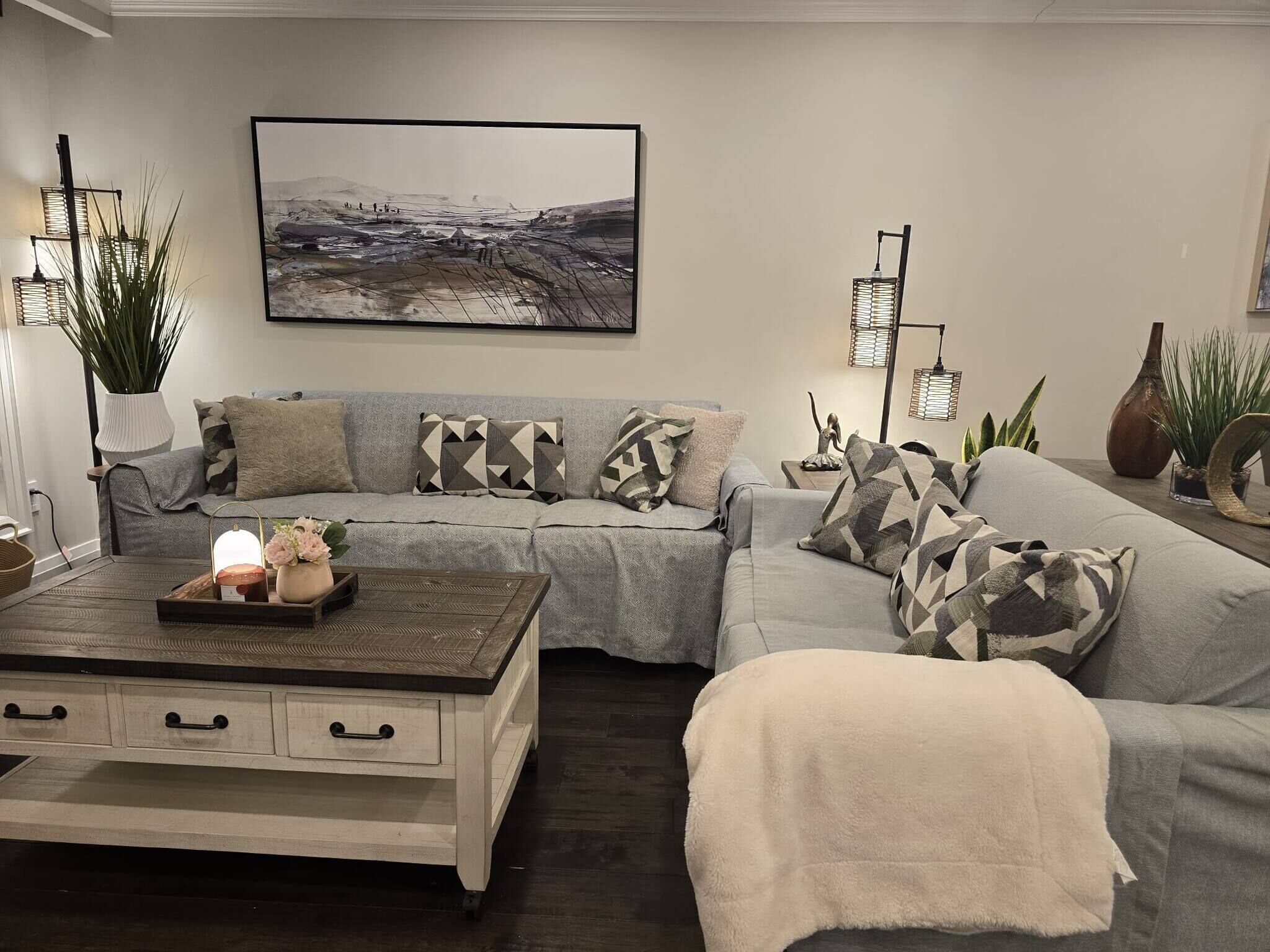 A modern living room with a grey sofa, a wooden coffee table, and a painting of a landscape.