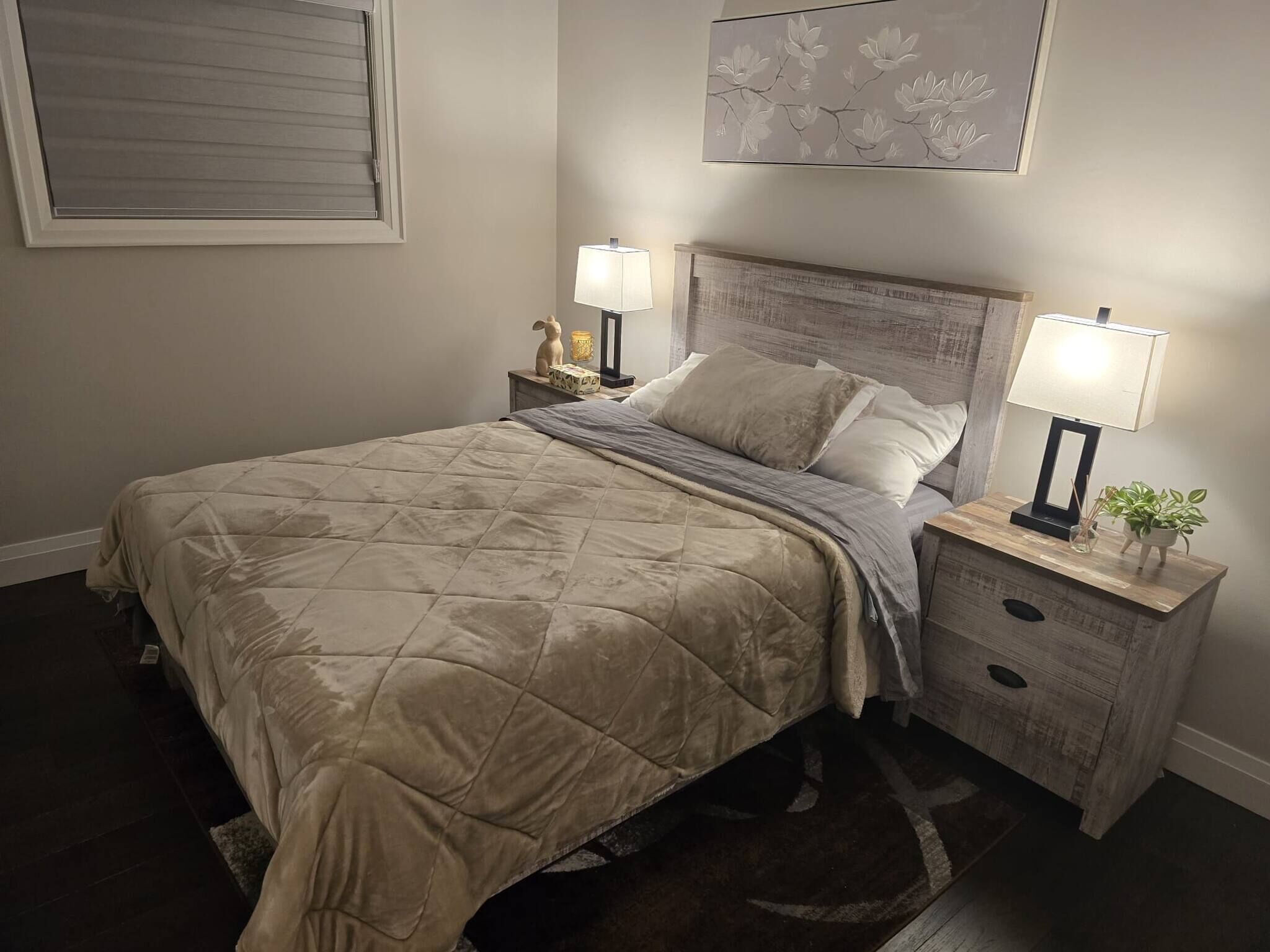 A bedroom with a bed, nightstands, a lamp, a plant, and a wall art piece.