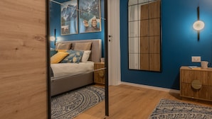 A bedroom with a bed, a wooden wardrobe, a mirror, and a blue wall with artwork. - Cheerful Apartment XX Settembre by Wonderful Italy (Turin)