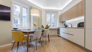 A modern kitchen with wooden cabinets, a dining table with chairs, a flat-screen TV, and a large window with a view of buildings. - Cheerful Apartment XX Settembre by Wonderful Italy (Turin)
