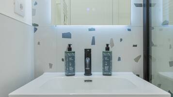Un baño con un lavamanos blanco, dos botellas de jabón para cabello y cuerpo, y un espejo encima.