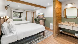 Ein Schlafzimmer mit zwei Betten, einer Holzbalkendecke, einem Spiegel, einem Fernseher und einem Badezimmer mit Waschbecken und Toilette.