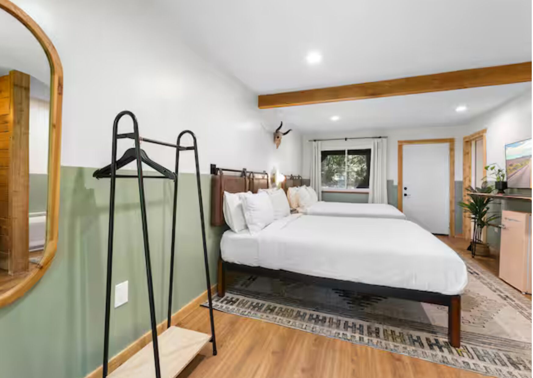 Een slaapkamer met een bed, een spiegel, een kapstok en een raam.
