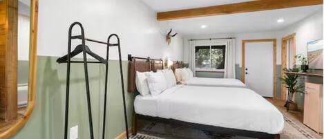 Een slaapkamer met een bed, een spiegel, een kapstok en een raam.