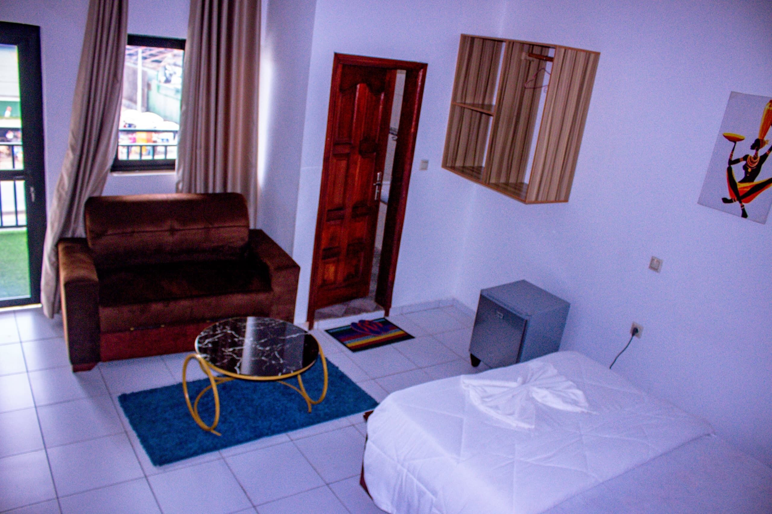 A room with a bed, a sofa, a small table, a TV, and a door leading to an outdoor area.