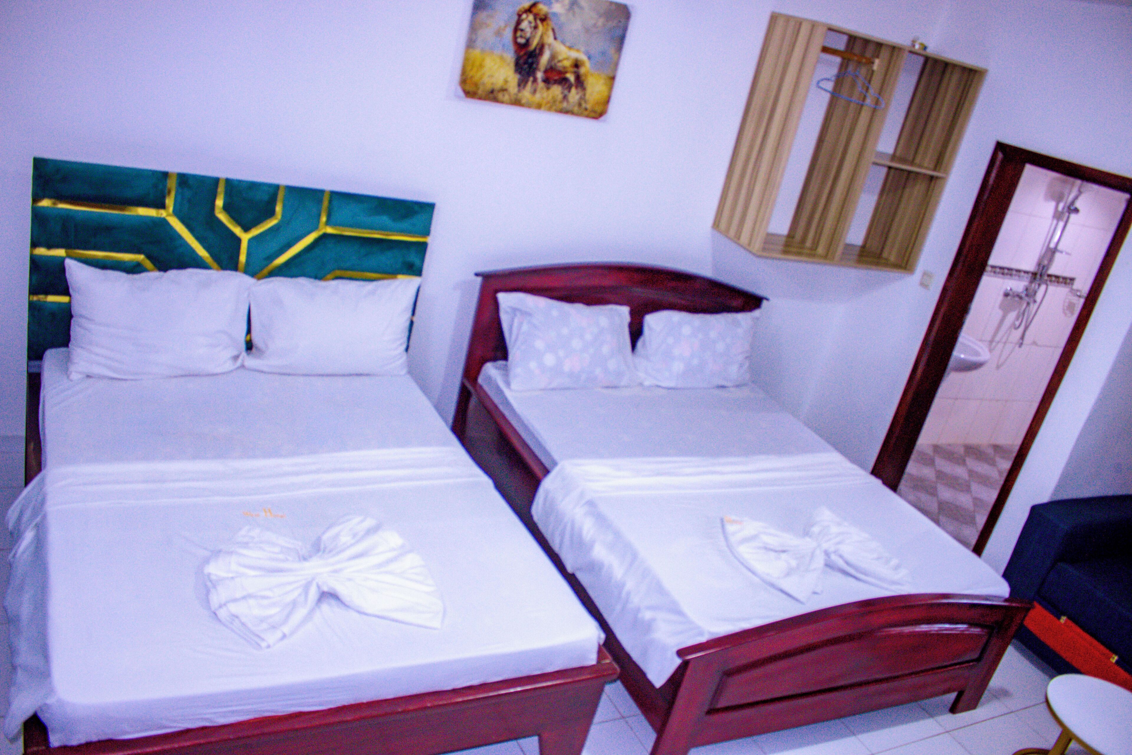 Two double beds with white linens and bows, a wooden headboard, a painting, a window with curtains, and a shower area.