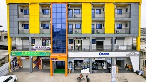 A multi-story hotel with a yellow facade, balconies, and a central glass elevator shaft. - WEST HOTEL DOUALA  (Bonaberi)