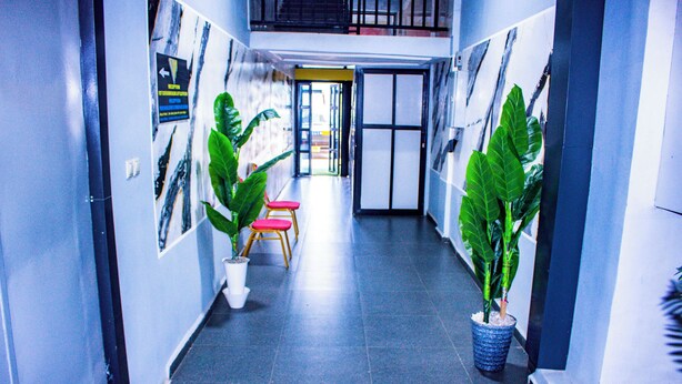 A hallway with potted plants, a red chair, and a door leading to another room. - WEST HOTEL DOUALA  (Bonaberi)