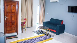 A living room with a sofa, a television, a door, and a window with curtains. - WEST HOTEL DOUALA  (Bonaberi)