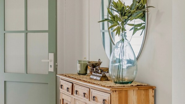 Une commode en bois sur laquelle sont posés un vase en verre contenant des plantes vertes, une bougie verte et un objet en métal.
