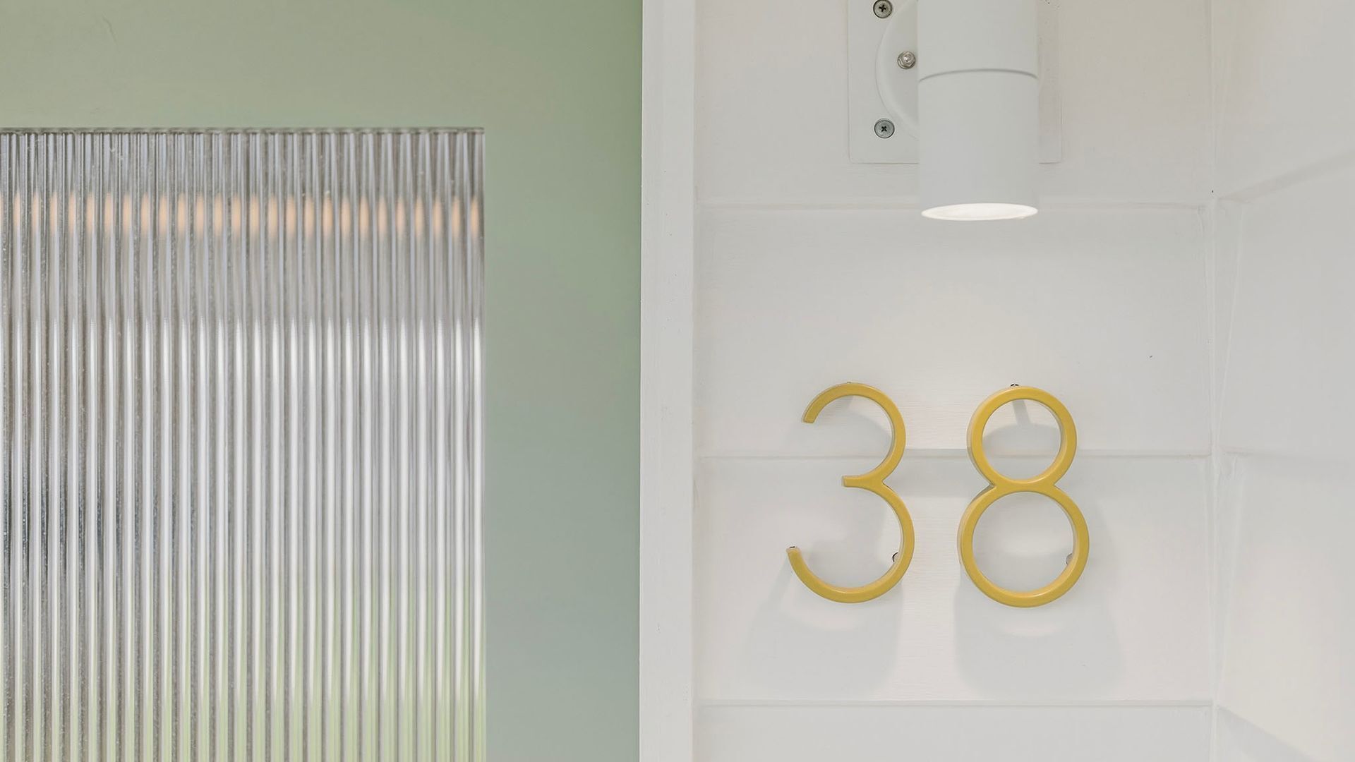 Una habitación con un separador metálico y acanalado, y una pared blanca con el número '38' en dorado.