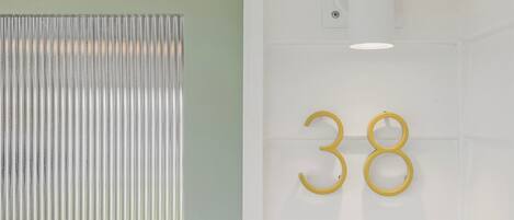 Una habitación con un separador metálico y acanalado, y una pared blanca con el número '38' en dorado.