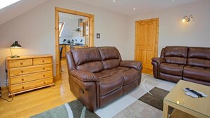 A modern living room with two leather sofas, a wooden dresser, and a glass coffee table. - Lochiel Apartment Self Catering (Fort William)