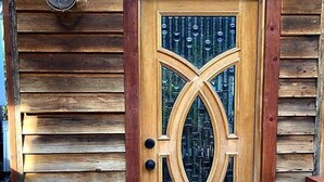 Puinen ovi, jossa on koristeellinen lasipaneeli ja sen yläpuolella metallinen valaisin.